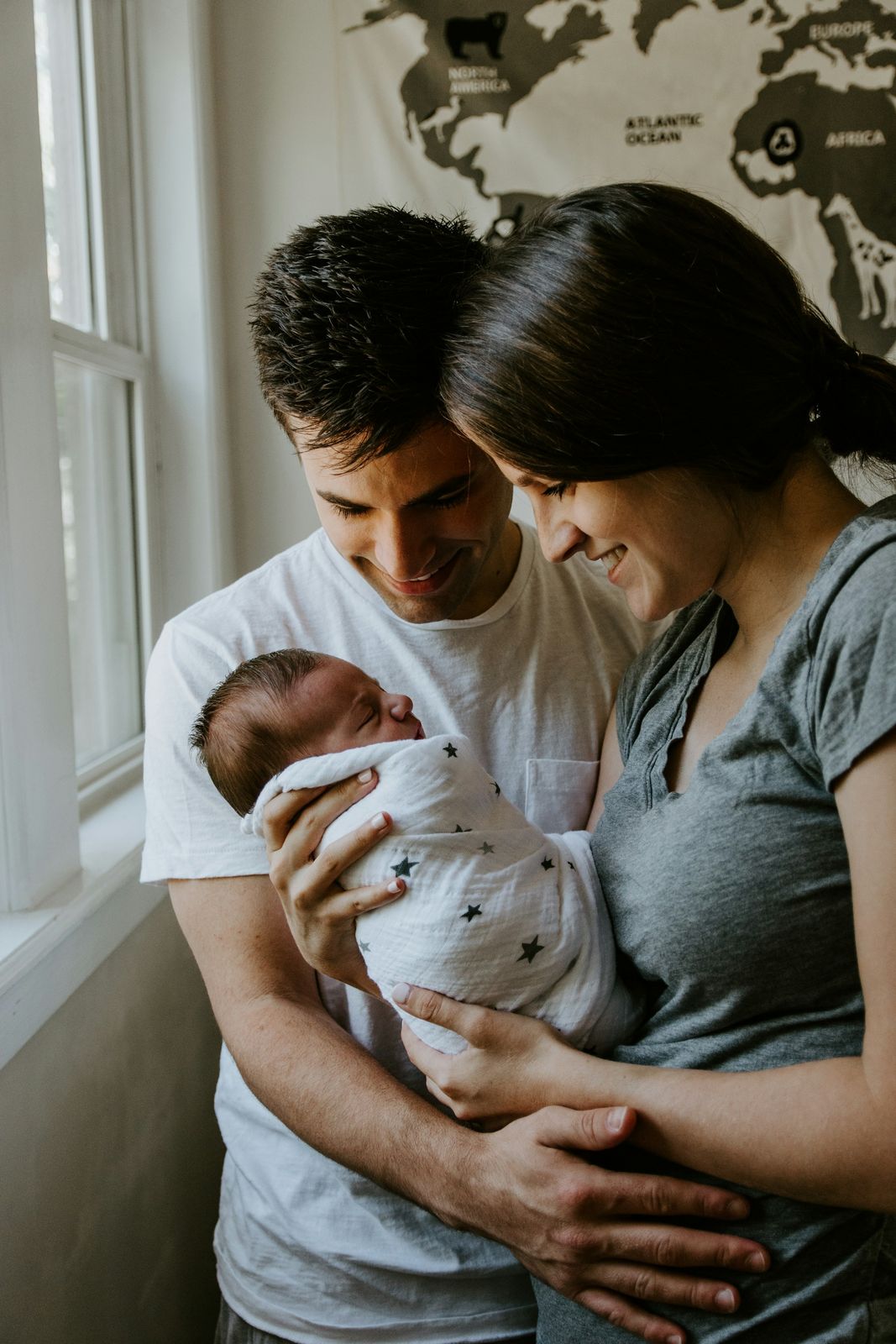 Parents holding their newborn baby beside a sunny window